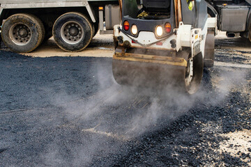 Construction workers in high-visibility gear are applyin gfresh hot asphalt to roadway surface