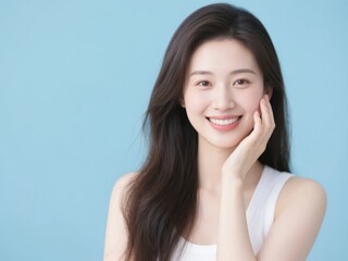 Fototapeta premium A person with long hair, wearing a white tank top, gently touching their face against a light blue background.