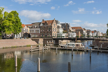 Obraz premium A picturesque scene in Gorinchem, Netherlands, showcasing traditional Dutch canal houses, the Peterbrug (Peter Bridge), and a house boat on the tranquil canal under a bright sky.