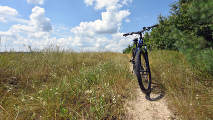Obraz premium bike stands on the road in the field. A mountain bike stands on a field path with dry grass. ride a bike. outdoor activities. autumn season. sports and outdoor recreation. active lifestyle, cycling.