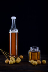 honey in a glass jar and bottles with longan fruit in black background
