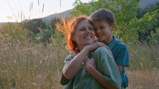 Happy mother and young son sharing joyful hug and laughter outdoors at golden hour. Authentic family bonding moment.