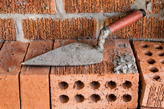 Close-up of rugged brick wall with loose bricks & trowel on building site