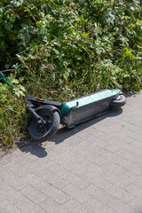 Abandoned e-scooter lying in grass by sidewalk