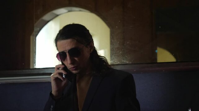 A serious and discreet mood is captured as a man in a suit and sunglasses talks on a mobile phone, with a digital clock in the background. This shot is ideal for depicting clandestine conversations