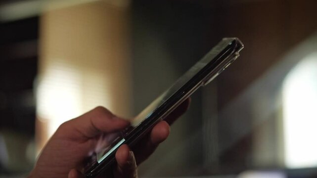 A focused and modern mood is captured as a hand holds a glowing smartphone, its screen reflecting light, against a softly blurred background. This shot is ideal for illustrating digital connectivity
