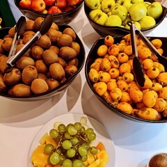 A colorful fruit display featuring ripe kiwi, loquats, green apples, and fresh grapes glows under...