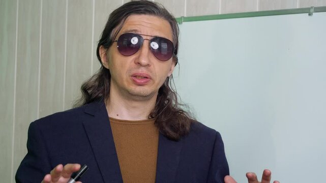 An authoritative and engaging mood is captured as a man in sunglasses and a suit jacket, holding a marker, gestures expressively while standing next to a whiteboard
