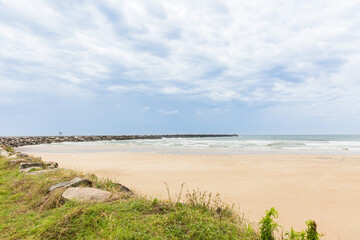 Rock wall curving around beach with sand and water and cloudy skies