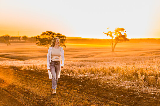 Teenage girl walking on dirt road against sunset rural landscape