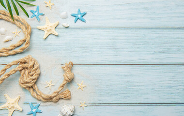Summer concept with palm leaf, rope, seashells and starfishes on light blue wooden background