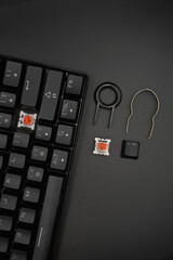 A black mechanical keyboard with a 61% layout with keycaps puller and switch puller and red...