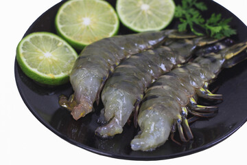 Close-up Fresh Black Tiger Shrimp without Heads with Shells on Black Plate with Thin Lime Slices and Thai Coriander on White Background – Clipping Path Included