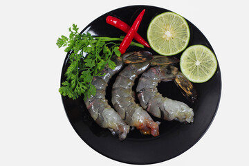 Fresh Black Tiger Shrimp without Heads and Shells Except Tails with Lime Slices, Chili, and Thai Coriander in Black Plate on White Background – Clipping Path Included