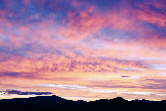 Silhouette of mountains under a dramatic sky at sunset. - Powered by Adobe