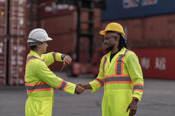 Two professional workers in neon reflective suits shake hands in a logistics hub, highlighting teamwork, agreement, and successful coordination in freight, transportation, and supply chain operations