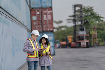 Two logistics workers asian man and woman discuss operations at a busy shipping container yard. One...
