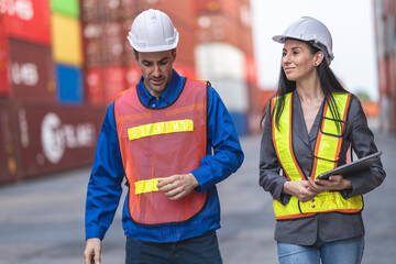 Two logistics workers man and woman discuss operations at a busy shipping container yard.