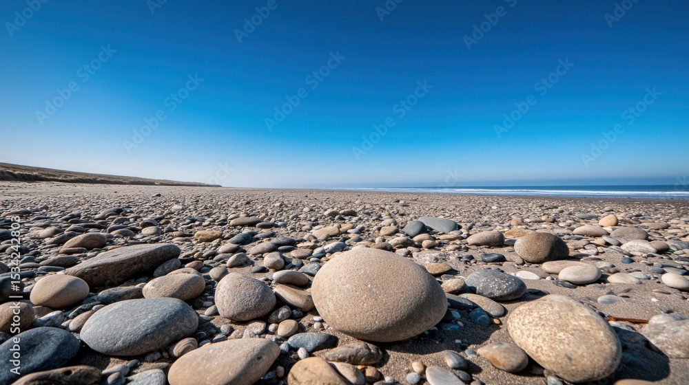 Poster a remote empty beach with large rocks and smooth pebbles scattered across the shore, under a clear b