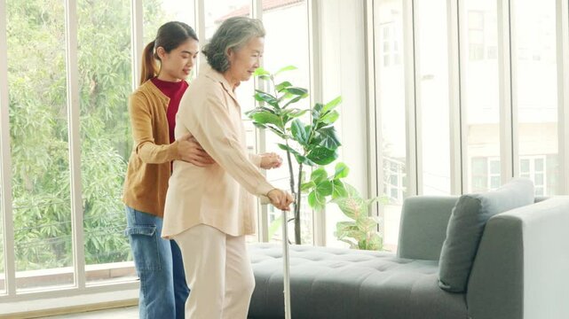 Female nurse who is taking care elderly woman with osteoarthritis needs cane help her walk to help her stand up and walk carefully and take care of her by being concerned and caring walk slowly.
