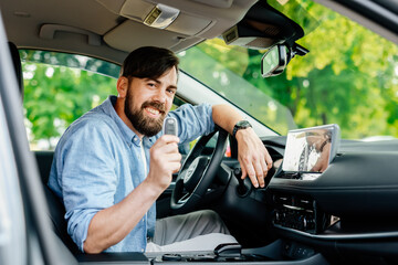 A happy young man sits in the passenger compartment of his brand new car and shows the keys to the...