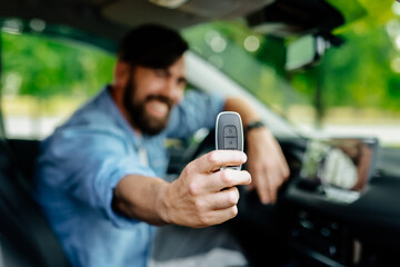 A happy young man sits in the passenger compartment of his brand new car and shows the keys to the...