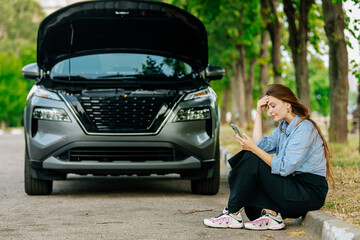 A young woman stands by her car, feeling confused and anxious, and calls for help on the phone. The...