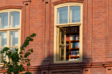An open library window, bookshelves, a red brick building facade