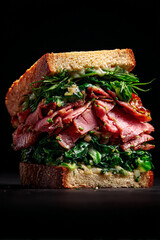 Close up of a sandwich with meat and green leafy vegetables on dark background