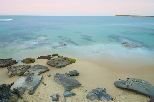 Beach, rocks and ocean at sunset with blurred motion of waves