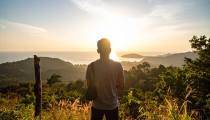 Fototapeta premium Man Silhouetted Against Sunset Over Ocean and Lush Hills.