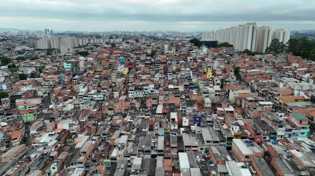 Drone image of an expansive favela in Osasco, S&atilde;o Paulo, Brazil, highlighting dense informal housing and urban inequality near high-rise buildings. 
