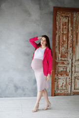 Fototapeta premium Pregnant woman in dress with very long hair on grey background. Dreamy tender girl expecting a child. Portrait of beautiful brunette pregnant woman. Window