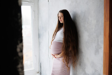 Pregnant woman in dress with very long hair on grey background. Dreamy tender girl expecting a...