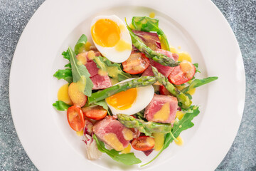 Elegant Niçoise portion with eggs, tuna, arugula, asparagus, cherry tomatoes, white plate
