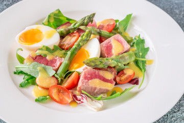 Elegant Niçoise portion with eggs, tuna, arugula, asparagus, cherry tomatoes, white plate