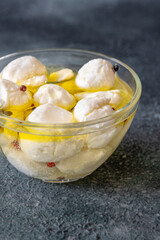 Glass bowl of labneh balls in oil, spiced with garlic and rosemary