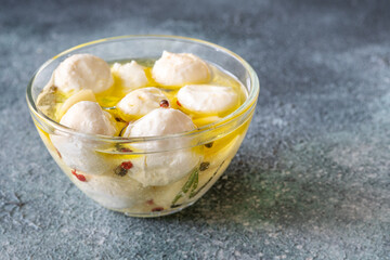 Glass bowl of labneh balls in oil, spiced with garlic and rosemary