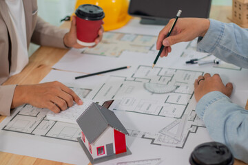 Architect and businessman discussing interior mansion plans using pencils and models at desk, including real estate purchase planning with leaders, marketing and engineering insights.