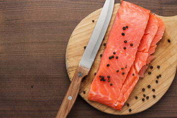 Seasoned trout and knife on the cutting board. Cutting board with fish on it on brown wooden table with copy space.