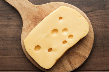 Flat lay photo of big piece of Swiss cheese on wooden cutting board.