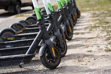 Photo of battery-powered rental scooters. Concept of new trends in sustainable urban transportation. Many electric scooters parked in a row in a sidewalk in the city. Rental business.