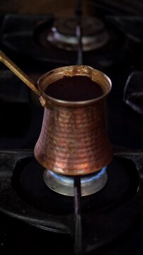 An aromatic and traditional mood is captured as dark, rich Turkish coffee simmers and brews in a classic copper cezve pot on a gas stove, with subtle steam rising