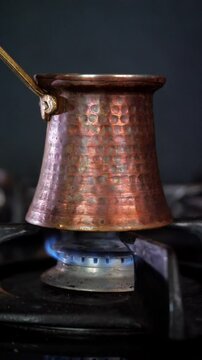 An aromatic and traditional mood is captured as dark, rich Turkish coffee simmers and brews in a classic copper cezve pot on a gas stove, with subtle steam rising
