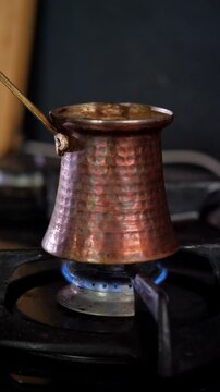 An aromatic and traditional mood is captured as dark, rich Turkish coffee simmers and brews in a classic copper cezve pot on a gas stove, with subtle steam rising