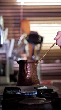 An authentic and aromatic mood is captured as Turkish coffee is brewed in a traditional cezve pot over a blue gas flame. This shot is ideal for depicting cultural culinary practices, the art of coffee