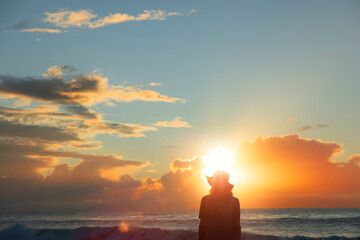 Silhouette eines jungen Mannes mit Hut bei Sonnenaufgang am Strand