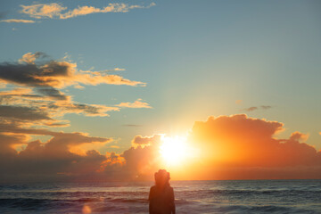 Silhouette eines jungen Mannes mit Hut bei Sonnenaufgang am Strand
