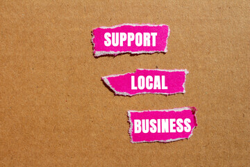 Support local business message written on ripped torn pink paper pieces on cardboard background. Conceptual support local business symbol. Copy space.