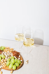 Two glasses of white wine and a wooden plate with cashews, pistachios, pecans and grapes on the dining table.